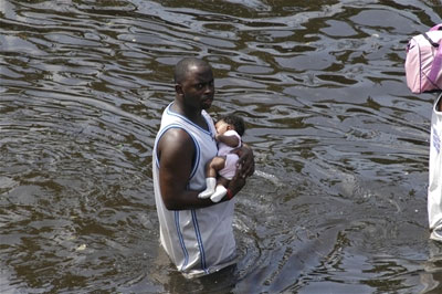 A father carefully holds his baby as he wades to safety